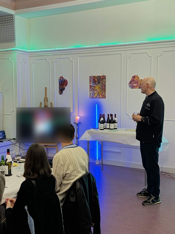 Gäste verfolgen eine Videobotschaft auf dem Bildschirm, daneben Reto Frey